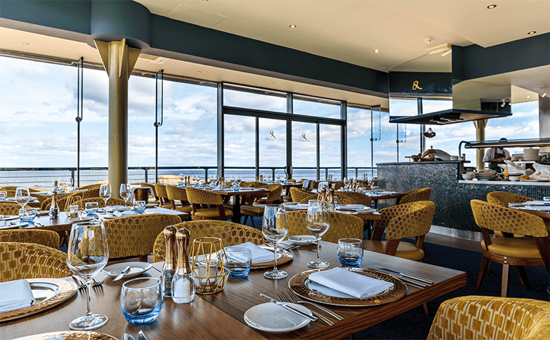 Low-backed gold chairs allow everyone to enjoy the sea views, while iridescent tiles and notes of blue add to the marine feel of the dining room