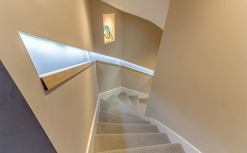 The stairway leading to the open-plan kitchen and dining area in the extension, its integrated lighting highlighting the minimal wooden banister