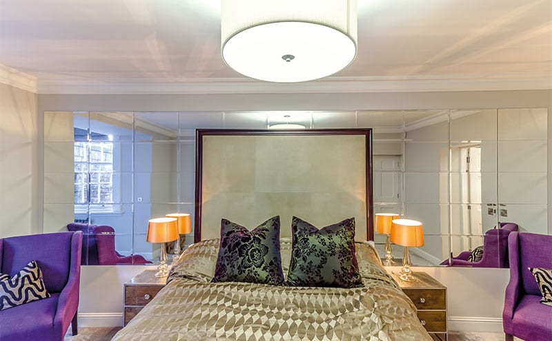 A sumptuous bright bedroom, its mirrored wall panelling reflecting light and space