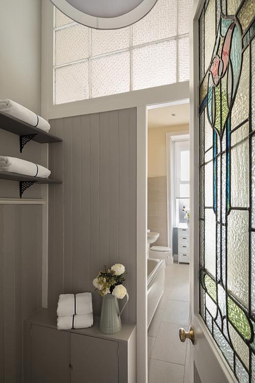 Simplicity rules in the bathroom, where a largely pale and neutral palette of colours and materials allows period details such as tongue-and-groove panelling and the stained-glass door to shine