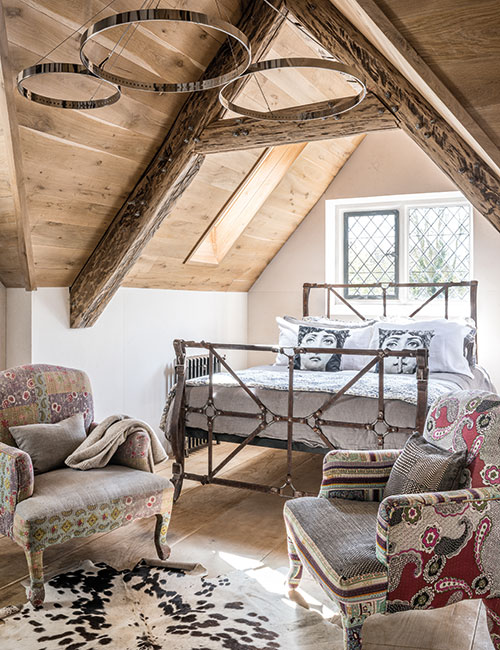 Reclaimed oak floorboards line the sloping ceiling of the guest bedroom. Vintage blue and white fabric on the bed (from And So To Bed) echoes the colours of the traditional Delft tiles which clad the chimney breast. The armchairs are upholstered in remnants of Indian prints