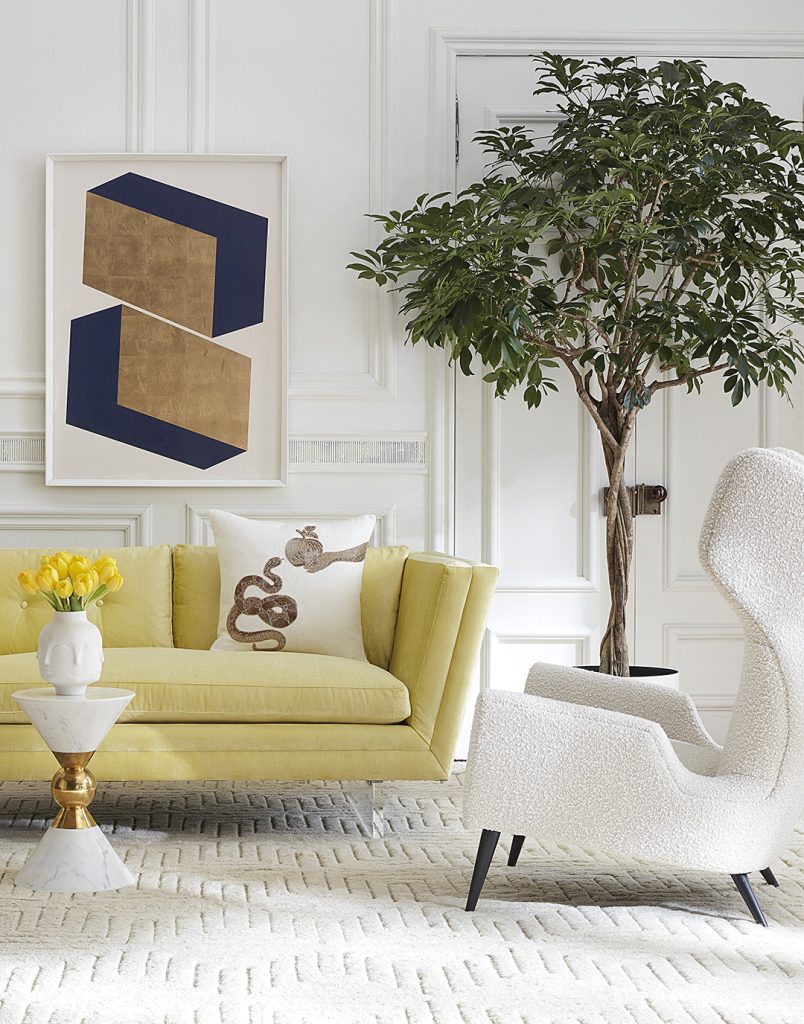 A light yellow sofa and a boucle white armchair sit on either side of a potted indoor tree